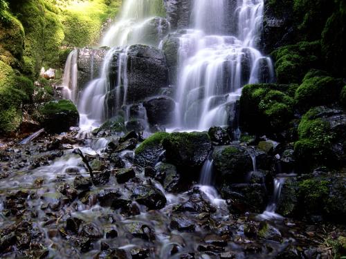 монументальный водопад с высокой горы в зеленую долину с черными камнями